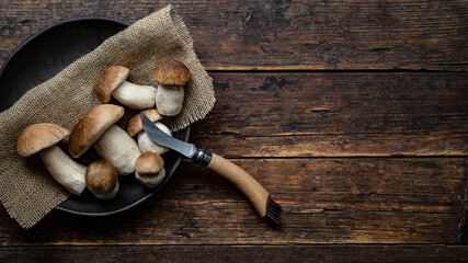 Fresh forest mushrooms /Boletus edulis (king bolete) / penny bun / cep / porcini / mushroom and knife in an old bowl / plate on the wooden dark brown table, top view background