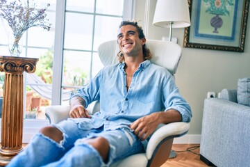 Wall Mural - Young hispanic man smiling happy sitting on the sofa at home