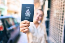 Young Beautiful Blonde Caucasian Woman Smiling Happy Outdoors On A Sunny Day Showing Canada Passport
