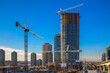 New construction of high-rise buildings in Burnaby city, industrial construction site, construction equipment, several construction cranes on the background of finished skyscrapers and a clean blue 