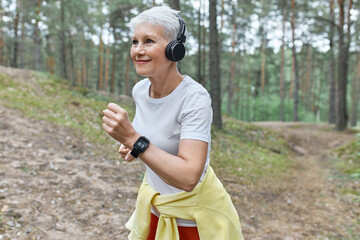 Old woman making sport. Running time in the forest with headphones and modern music. Happy and health time for grandmother. Feel power. Fitness concept.