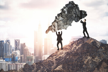 Canvas Print - Two businessmans standing on mountain top and holding rock