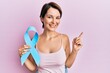 © Krakenimages.com - Young brunette woman with short hair holding blue ribbon smiling happy pointing with hand and finger to the side