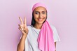 © Krakenimages.com - Young brunette woman wearing breast cancer support pink scarf smiling with happy face winking at the camera doing victory sign. number two.
