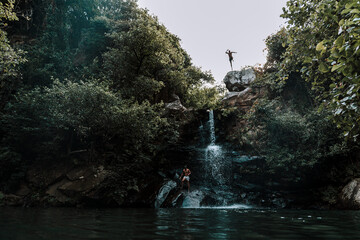 Chico saltando desde lo alto de una cascada al lago