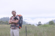 © AungMyo - Young man with backpack and holding a binoculars standing on top of mountain