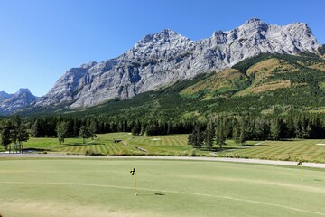 Wall Mural - Gorgeous putting green surrounded by forest and big mountains in the background, on a beautiful sunny day in Kananaskis, Alberta, Canada.