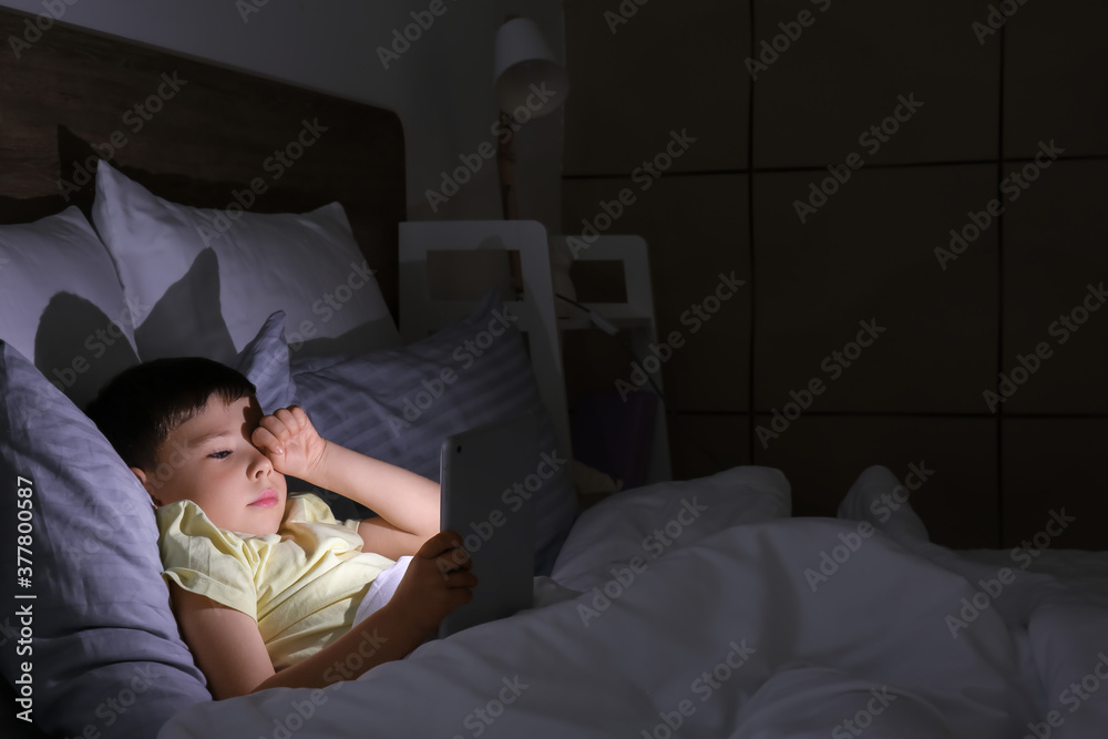Little boy suffering from sleep disorder with tablet computer in bedroom