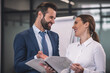 © zinkevych - Brown-haired female with bearded male colleague reading papers, discussing, smiling