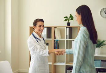 Smiling woman doctor shaking hand to woman patient after consultation in medical clinic office