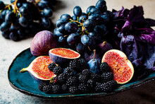 Purple Fruits And Berries In Blue Dish, Gray Background. Purple Food Background. Figs, Grapes, Plums And Blackberries In A Ceramic Plate.