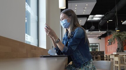 Wall Mural - Young woman sitting at coffee shop and connected with smartphone, wearing face mask