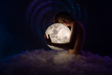 Wall Mural - tender young beautiful naked girl siting on the soft clouds and hugs the bright moon. girl's chest t