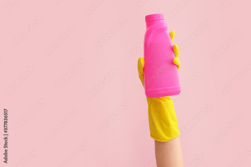 Hand in rubber glove holding detergent on color background