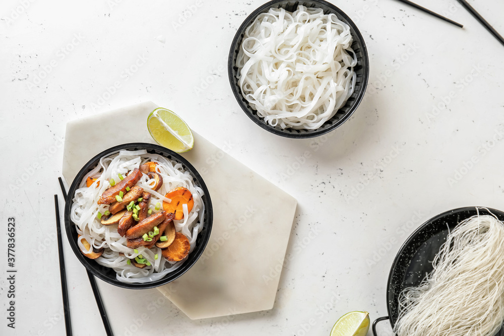 Bowls with tasty rice noodles and meat on white background