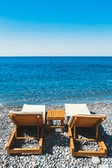 Two wooden sun loungers on the pebbled seaside - empty sun loungers in the resort - relaxation for a couple