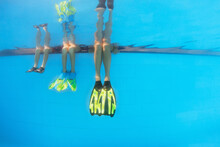 Happy People Have Fun At Pool Side Edge. Funny Photo Of Mother With Kids Legs In Fins In Aqua Park Swimming Pool. Family Lifestyle, Children Water Sport Activity, Lesson With Parents On Summer Holiday