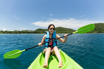 Happy woman with lifejacket kayaking in tropical island ocean on vacation.