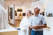 © caftor - mature European couple examines paintings in an exhibition in hall of art museum