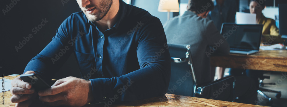 Business office concept. Portrait of handsome manager working at the table with mobile phone. Three employees at background. Wide screen, panoramic - obrazy, fototapety, plakaty 