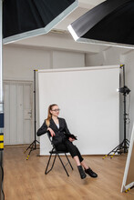 Business Vlog. Shooting Backstage. Creative Woman Posing Sitting In Modern Studio With Light Equipment White Backdrop. Professional Photography.