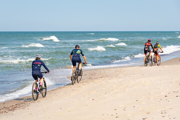 Cyclists with bikes riding on a beautiful sandy beach with rough Baltic Sea on background