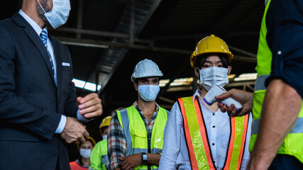 Industrial worker and engineer stand in line to check flu with infrared thermometer before enter to work and protect Coronavirus or Covid-19, safety and protection as working in manufacturing