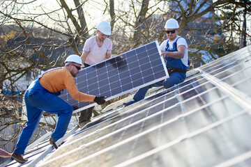 Wall Mural - Male team workers installing solar photovoltaic panel system. Electricians lifting blue solar module on roof of modern house. Alternative energy ecological concept.