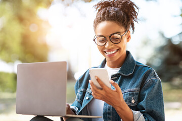 African Girl Texting On Smartphone Learning Using Laptop Sitting Outdoors