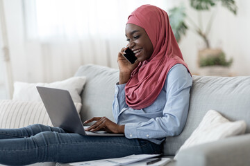 Black Muslim Lady In Hijab Working With Laptop And Cellphone At Home