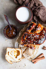 Poster - Apricot jam twisted loaf bread or babka with nuts and spices on concrete background with a cup of milk. Homemade yeast bun babka. Top view.