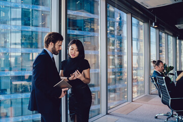 Wall Mural - Successful woman formally dressed showing video about financial job during communication with male partner, diverse colleagues connecting to office wifi on modern technology reading trade news