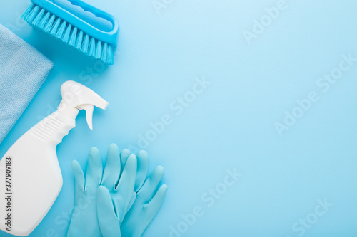 White bottle, rag, rubber protective gloves and brush. Cleaning set for different surfaces in kitchen, bathroom and other rooms. Light blue background. Top down view. Empty place for text or logo.