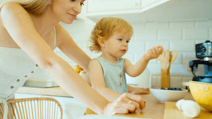 Young beautiful mother spending time with baby daughter in a kitchen. 