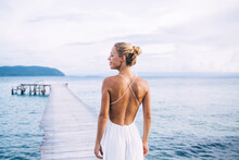 Back View Of Caucasian Female Tourist Enjoying Resort Vacations In Paradise Nature Environment, Attractive Woman Standing At Pier Recreation During Solo Travelling For Visiting Zanzibar Island