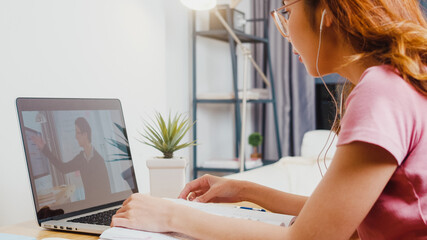 back view of young asia teen girl student wears headphones distance learning lesson with online teac