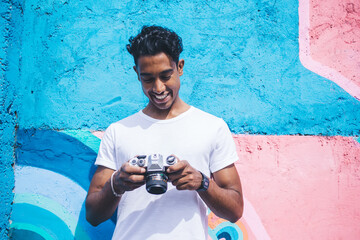 Smiling ethnic man watching pictures on camera screen in street