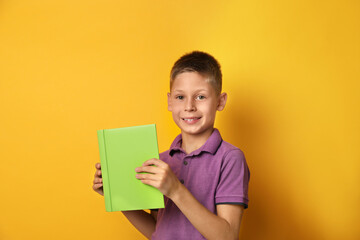 Wall Mural - Happy little boy with book on yellow background