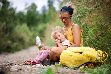 Wall Mural - mother with small toddler daughter hiking outdoors in summer nature, resting.