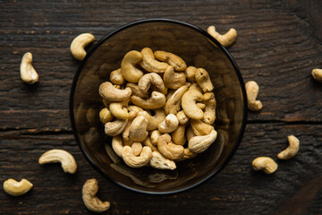 Wall Mural - Cashew nuts in a small plate with scattered cashew around a plate on a vintage wooden table as a background. Cashew nut is a healthy vegetarian protein nutritious food.