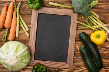 Wall Mural - top view of fresh ripe vegetables and empty chalkboard on wooden background
