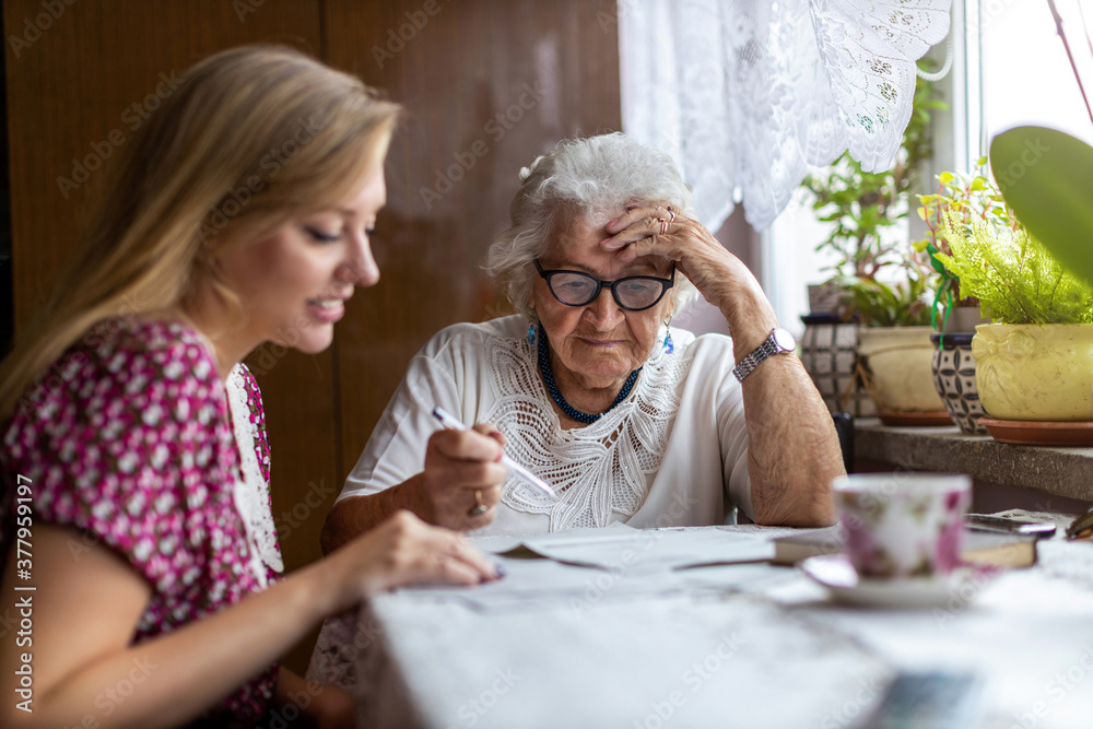Young woman helping elderly grandmother with paperwork
 - obrazy, fototapety, plakaty 