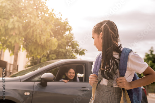 The girl turns to look at her mother who is staying in the car. Concept of school routine and transportation by private car.
