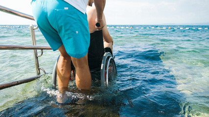 Wall Mural - Disabled man at beach swimming on a wheelchair with assistance help on an accessible ramp.