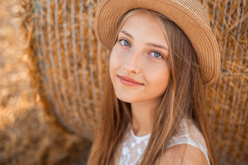 Sticker - Close-up portrait of a young girl in a light white dress and a hat near the straw bale