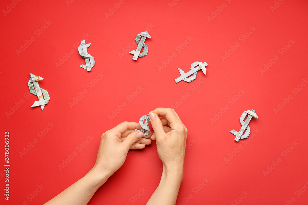 Woman making origami figures from dollar banknotes on color background