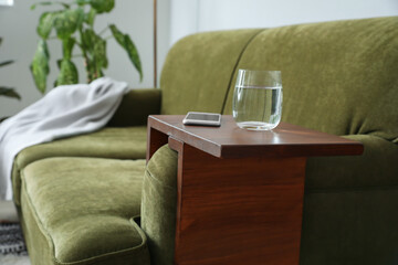 Glass of water with mobile phone on armrest table in room