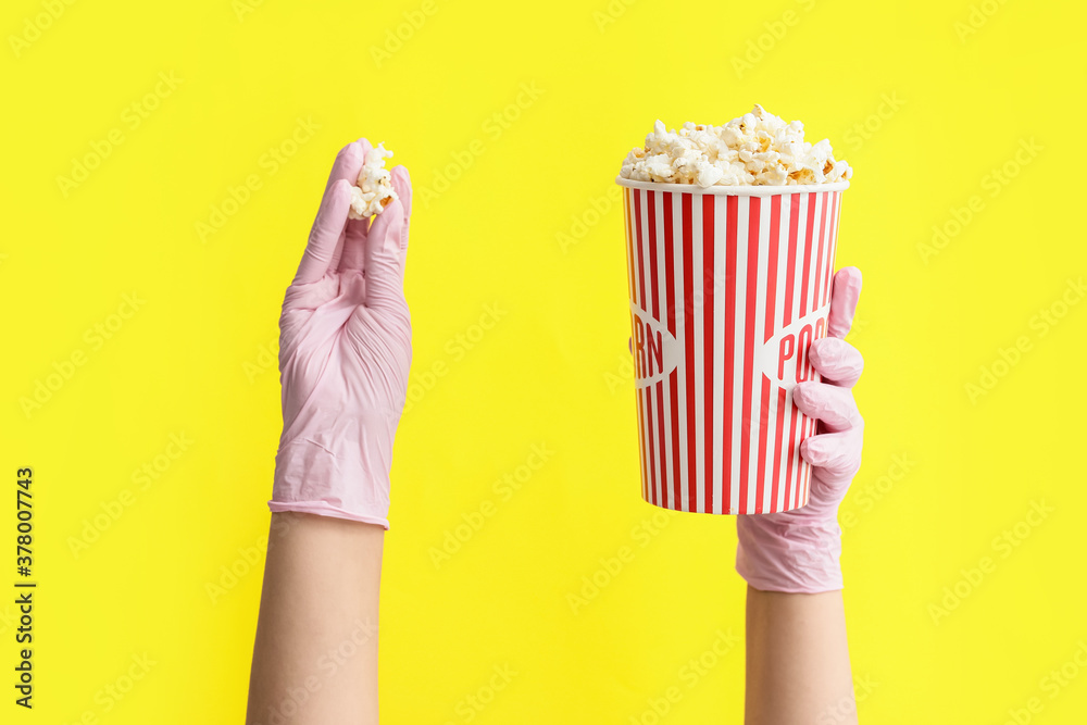Hands in protective gloves and with popcorn on color background