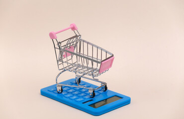 Market cost. Mini shopping trolley with calculator on beige background