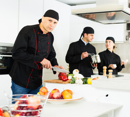 Man kitchener in uniform is cutting vegetables for salad in the kitchen at the restaurant.